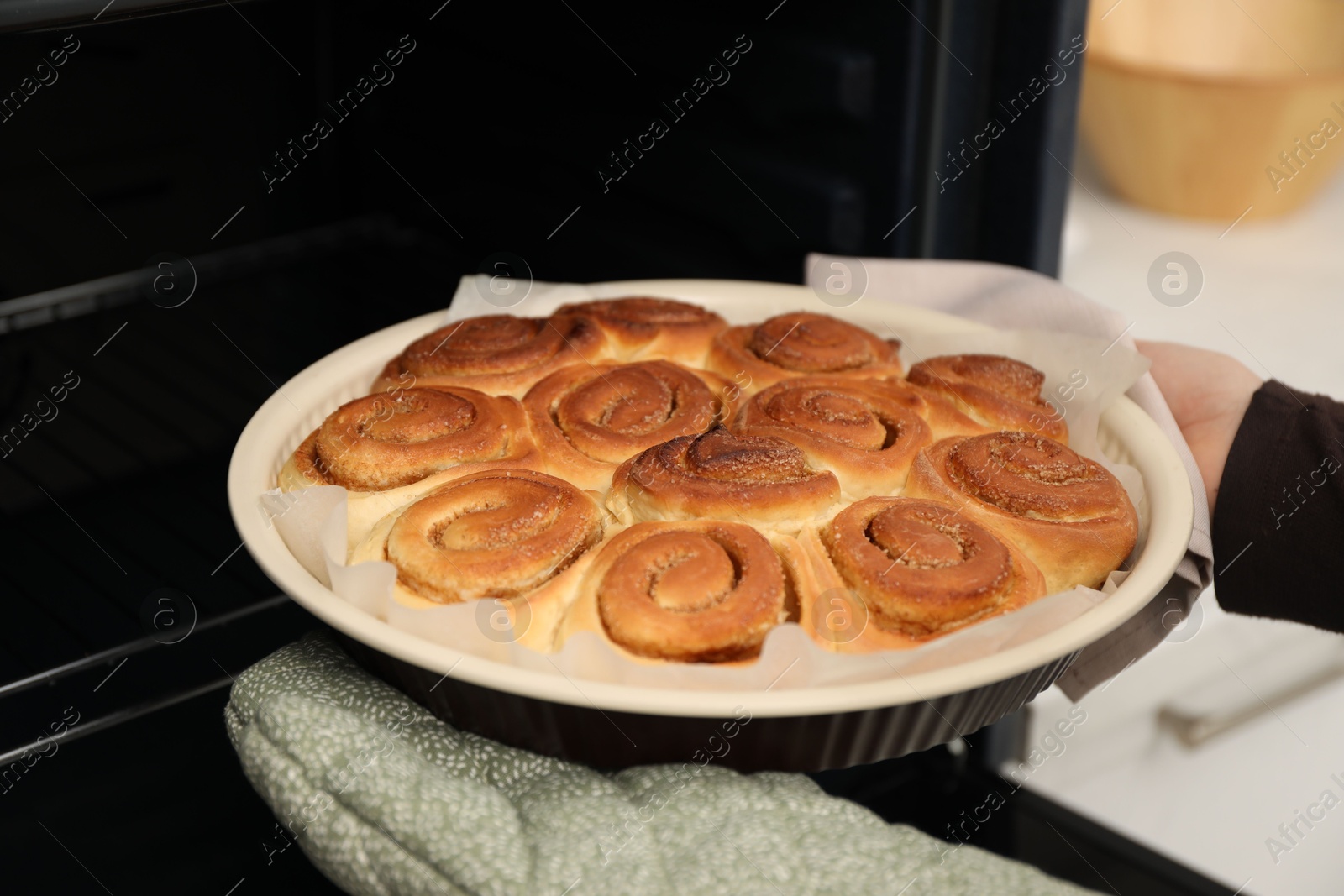 Photo of Woman taking delicious cinnamon rolls out of oven, closeup