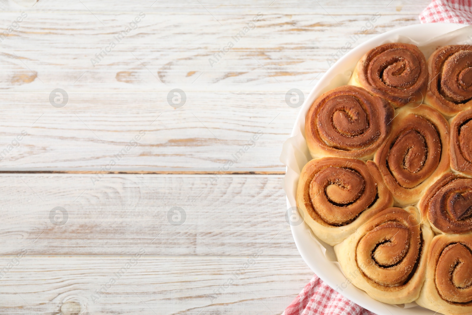 Photo of Freshly baked cinnamon rolls on light wooden table, top view. Space for text