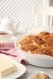 Photo of Freshly baked cinnamon rolls and ingredients on light wooden table indoors, closeup