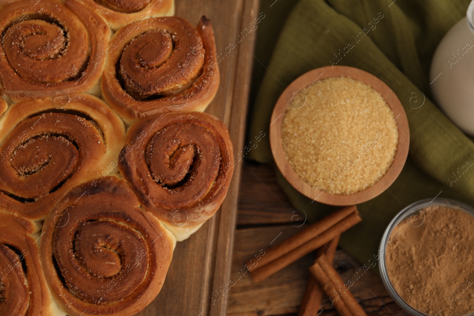 Photo of Freshly baked cinnamon rolls and spices on wooden table, flat lay