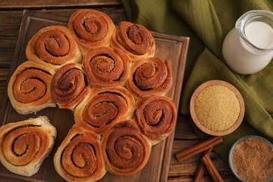 Photo of Freshly baked cinnamon rolls, milk and spices on wooden table, flat lay