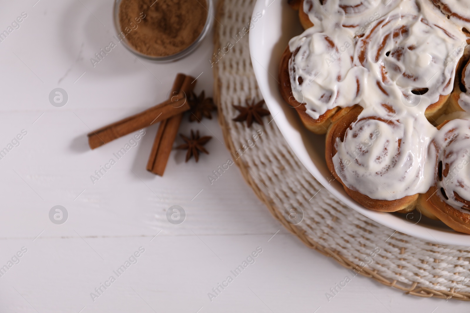 Photo of Delicious frosted cinnamon rolls and spices on white wooden table, flat lay. Space for text