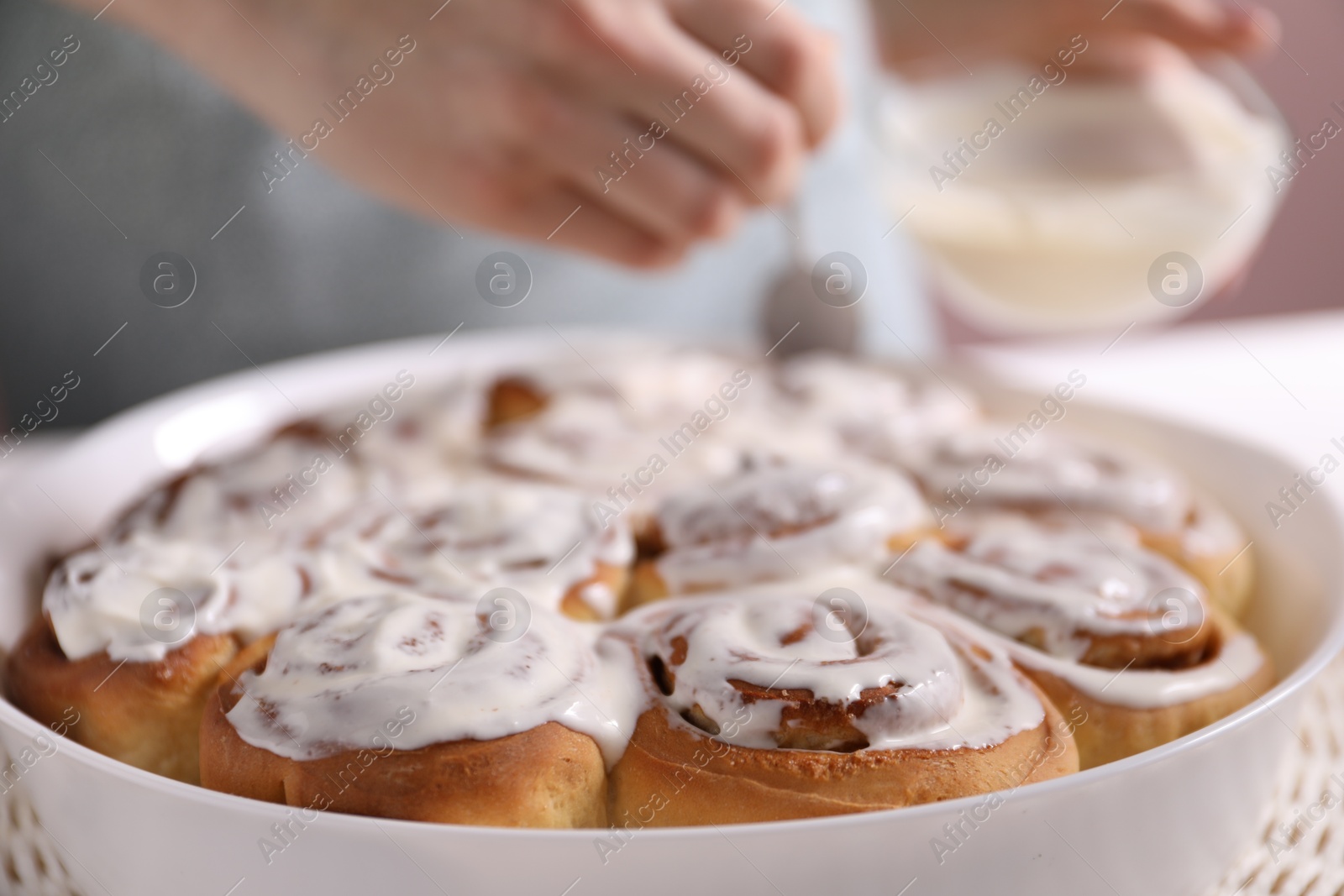 Photo of Delicious frosted cinnamon rolls and woman at table, selective focus