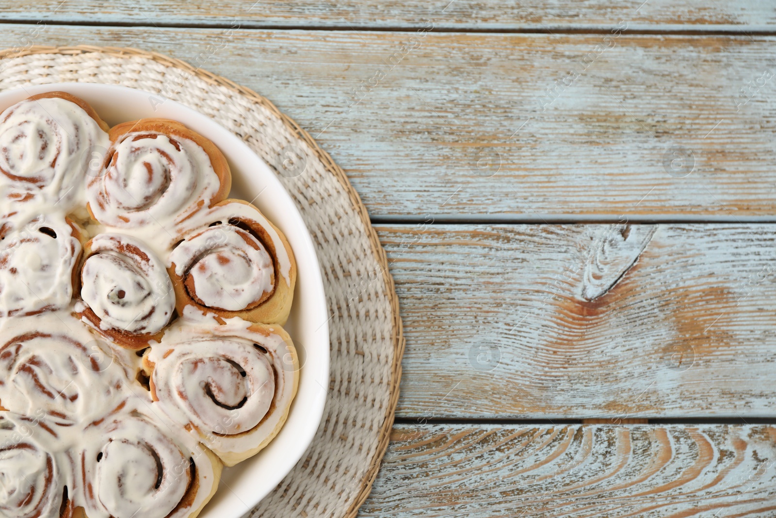 Photo of Delicious frosted cinnamon rolls in baking dish on wooden rustic table, top view. Space for text