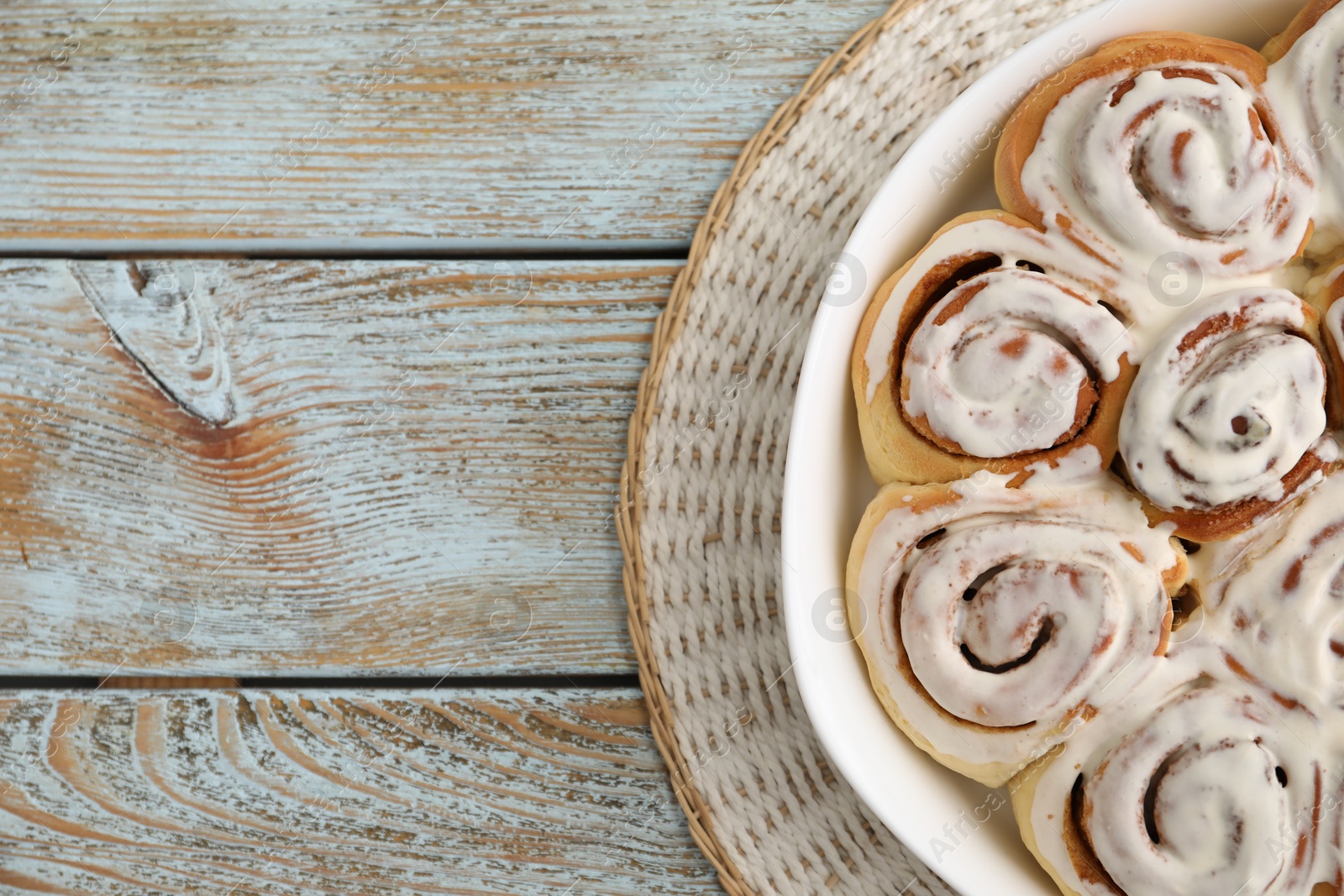 Photo of Delicious frosted cinnamon rolls in baking dish on wooden rustic table, top view. Space for text