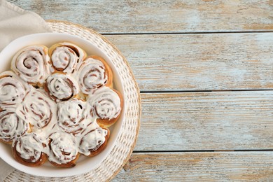 Photo of Delicious frosted cinnamon rolls in baking dish on wooden rustic table, top view. Space for text