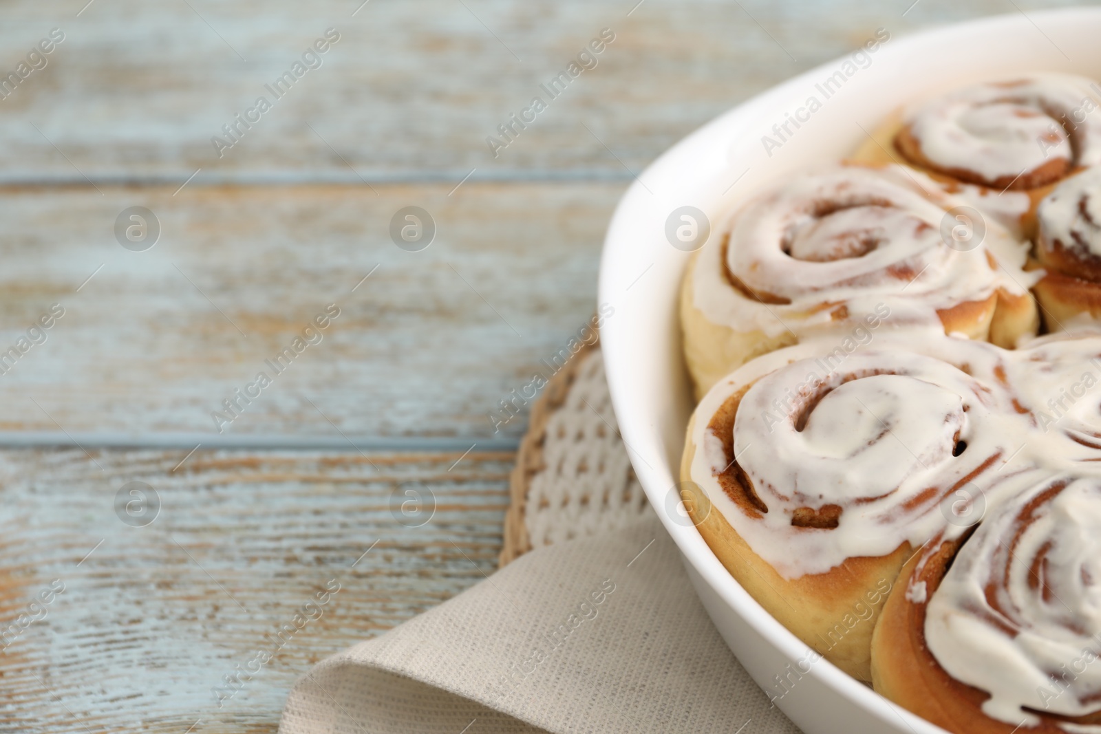 Photo of Delicious frosted cinnamon rolls in baking dish on wooden rustic table, closeup. Space for text