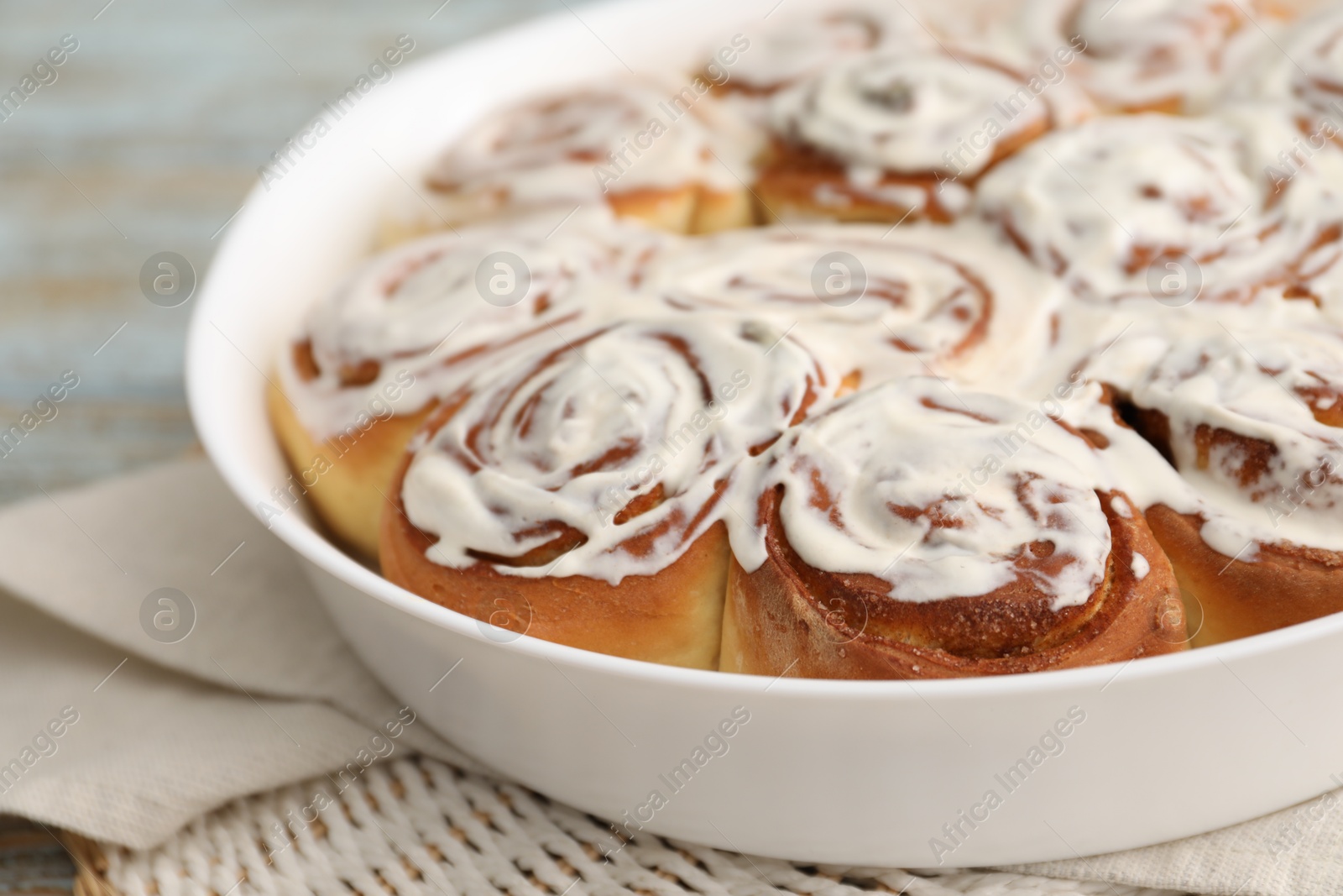 Photo of Delicious frosted cinnamon rolls in baking dish on table, closeup