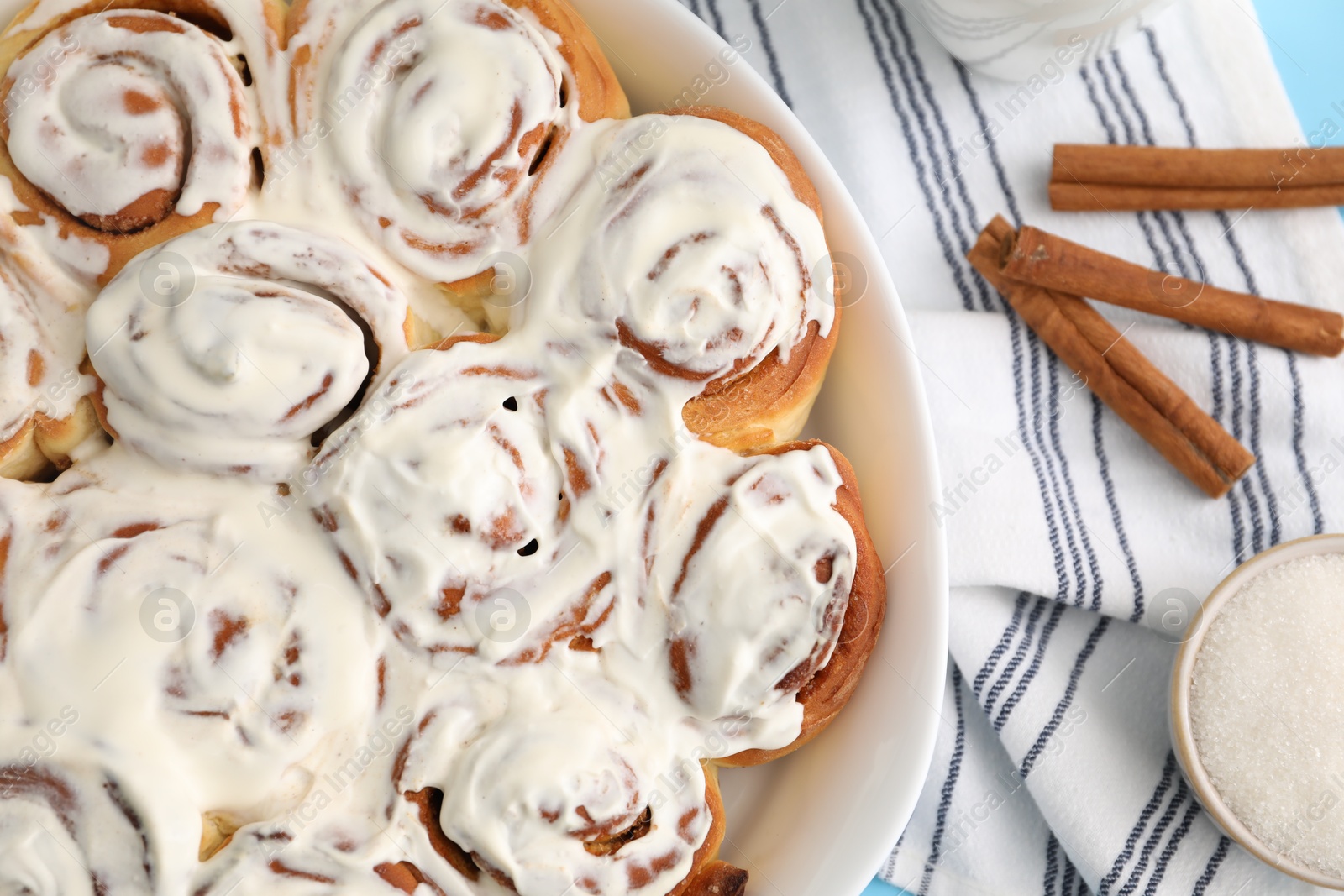 Photo of Delicious frosted cinnamon rolls in baking dish and spices on table, top view