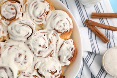 Photo of Delicious frosted cinnamon rolls in baking dish and spices on table, top view