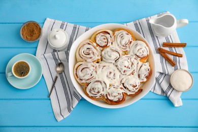 Photo of Delicious frosted cinnamon rolls in baking dish, coffee, milk and spices on light blue wooden table, flat lay