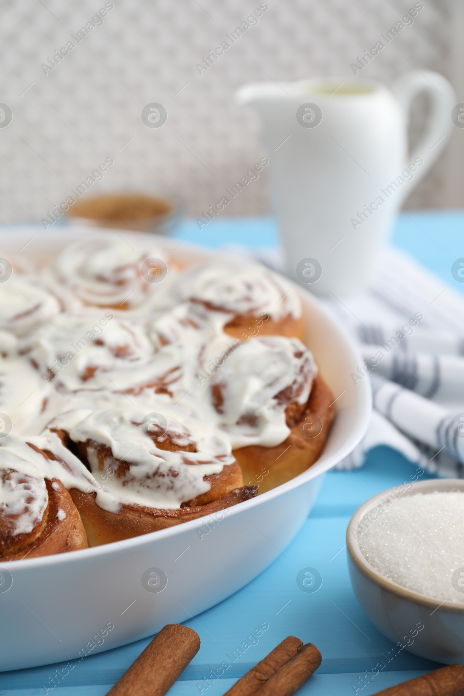 Photo of Delicious frosted cinnamon rolls in baking dish on light blue wooden table, closeup