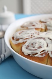 Photo of Delicious frosted cinnamon rolls in baking dish on light blue table, closeup