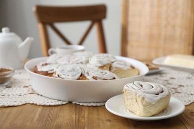 Photo of Delicious frosted cinnamon rolls on wooden table indoors, closeup