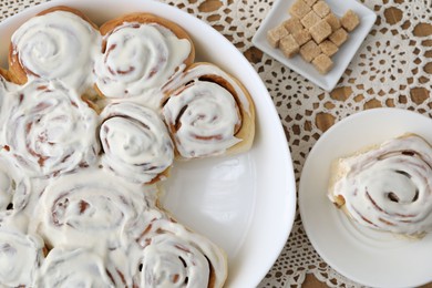 Photo of Delicious frosted cinnamon rolls and cubes of brown sugar on wooden table, top view