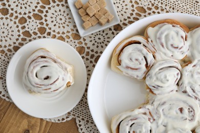 Photo of Delicious frosted cinnamon rolls and cubes of brown sugar on wooden table, top view