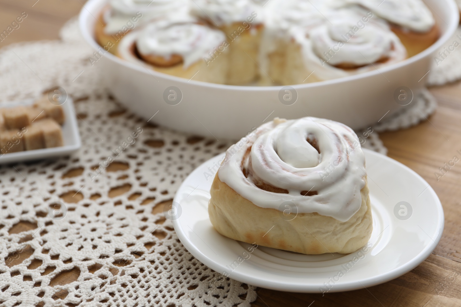 Photo of Delicious frosted cinnamon roll on wooden table, closeup