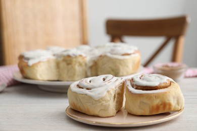 Photo of Delicious frosted cinnamon rolls on light wooden table indoors, closeup