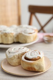 Photo of Delicious frosted cinnamon rolls on light wooden table indoors, closeup