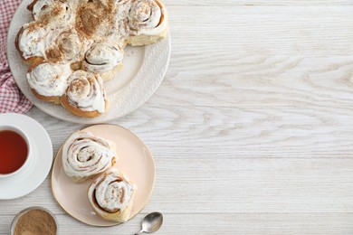 Photo of Delicious frosted cinnamon rolls and tea on light wooden table, flat lay. Space for text