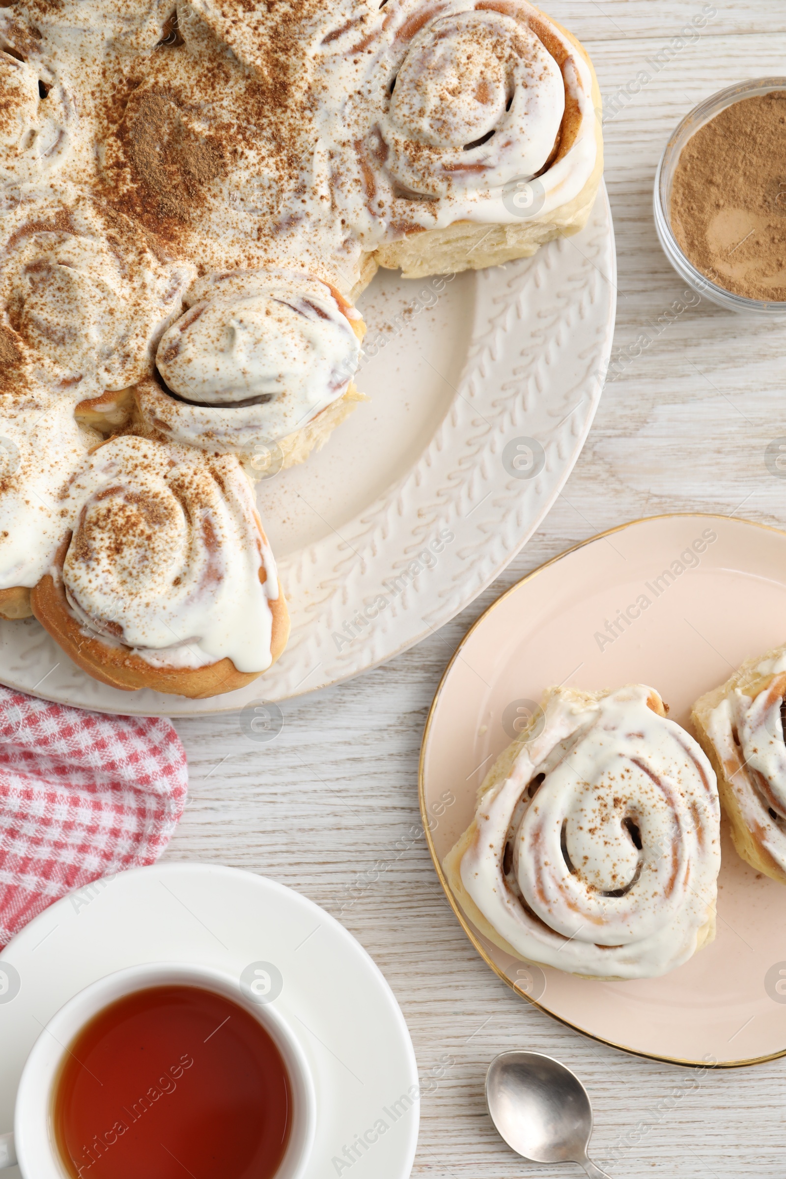 Photo of Delicious frosted cinnamon rolls and tea on light wooden table, flat lay