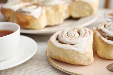 Photo of Delicious frosted cinnamon rolls and cup of tea on light wooden table, closeup