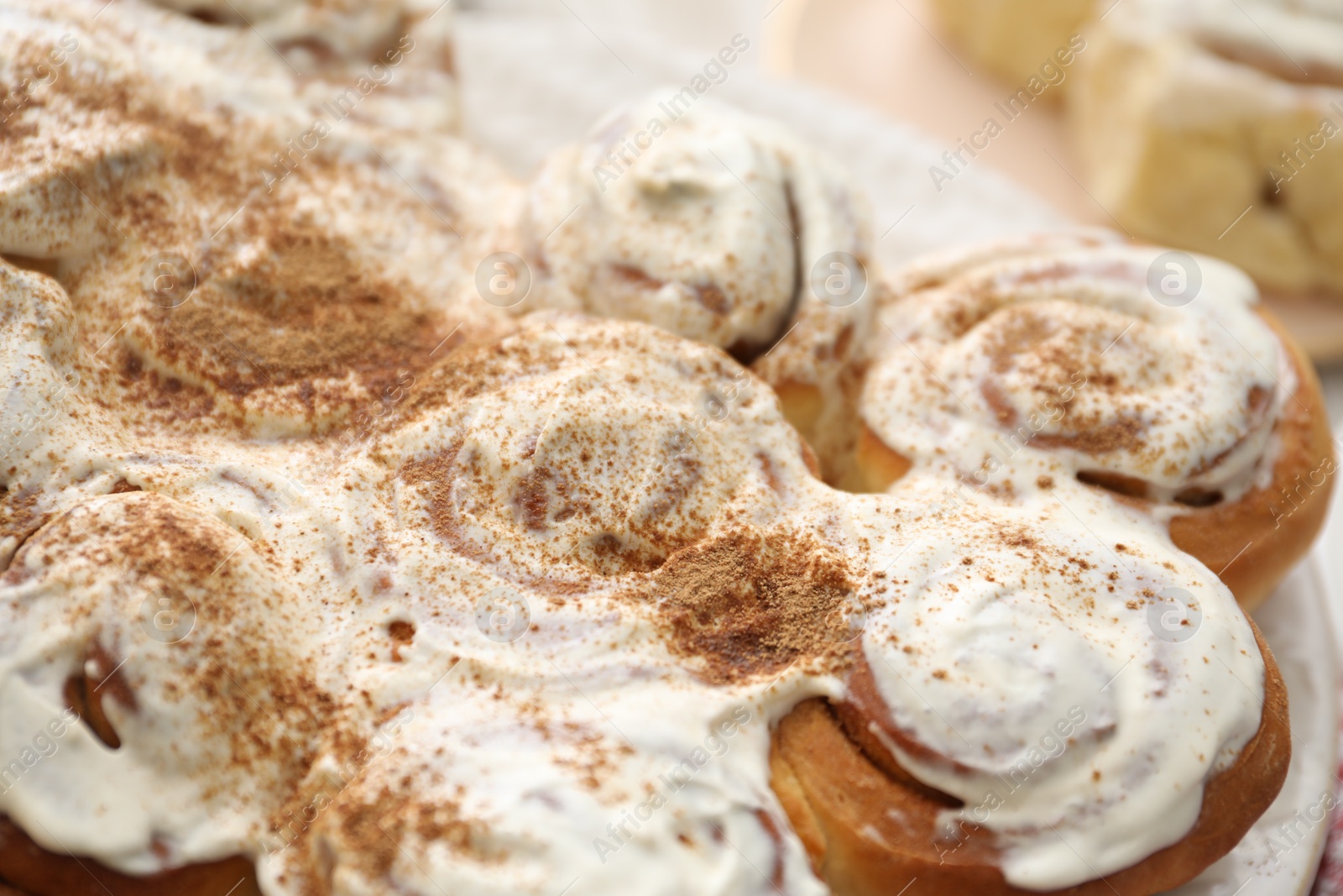 Photo of Delicious frosted cinnamon rolls on blurred background, closeup