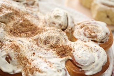 Delicious frosted cinnamon rolls on blurred background, closeup