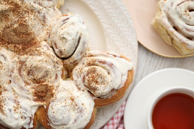 Photo of Delicious frosted cinnamon rolls and tea on light wooden table, flat lay