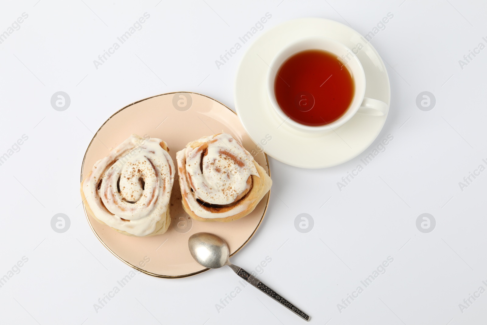 Photo of Delicious frosted cinnamon rolls and tea on white table, flat lay