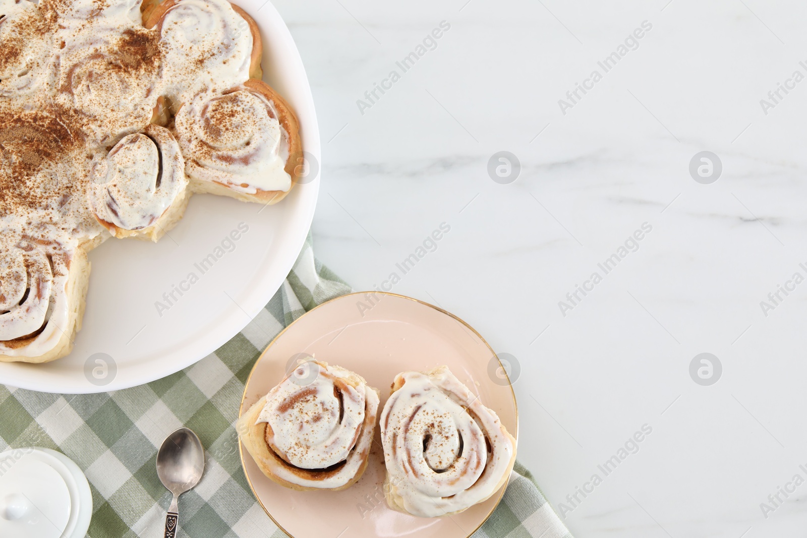 Photo of Delicious frosted cinnamon rolls on white marble table, top view. Space for text