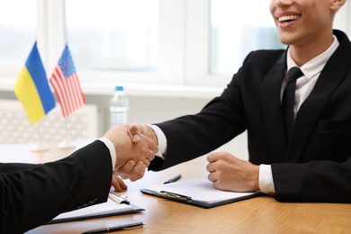 Diplomats shaking hands during meeting at wooden table indoors, closeup