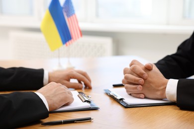 Photo of Diplomats negotiating during meeting at wooden table indoors, closeup