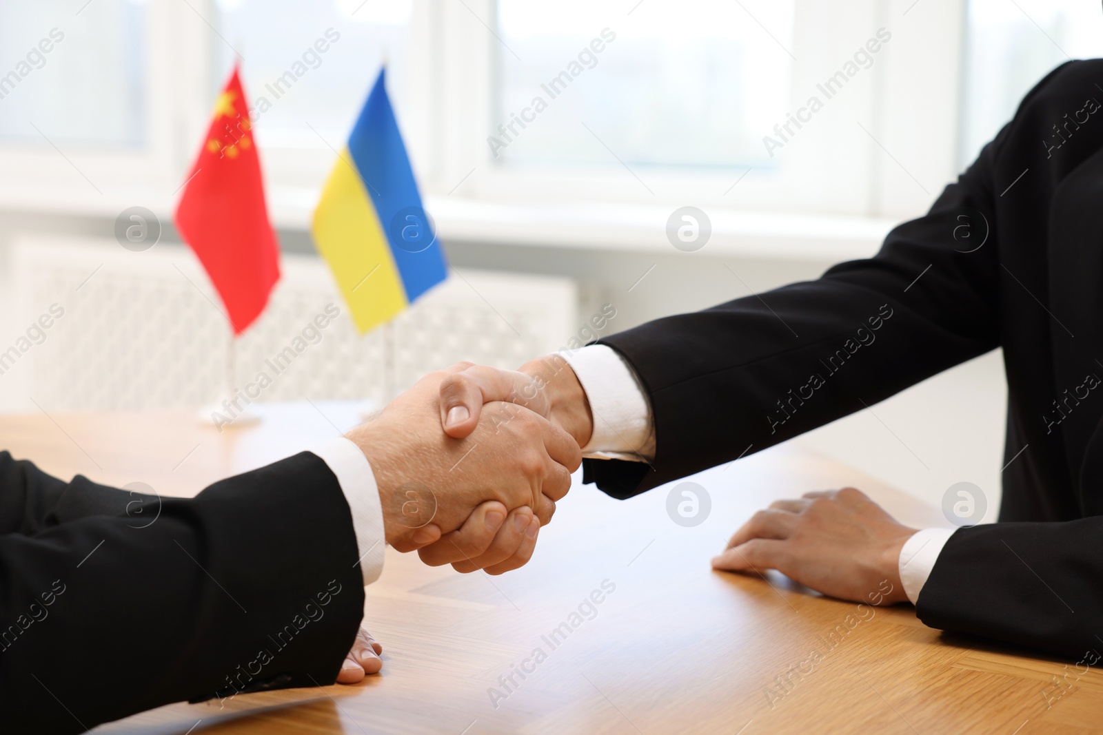 Photo of Diplomats shaking hands during meeting at wooden table indoors, closeup