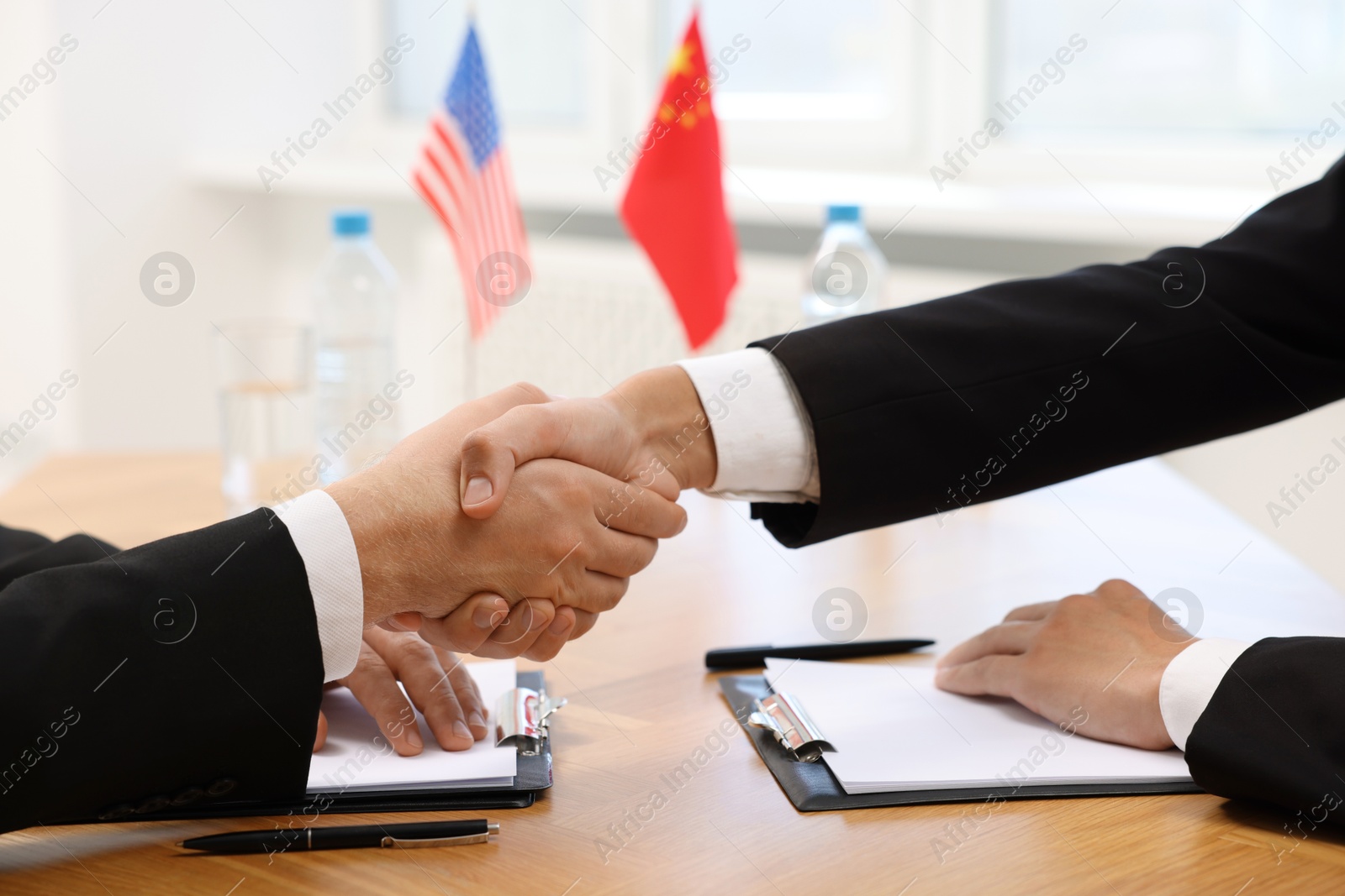 Photo of Diplomats shaking hands during meeting at wooden table indoors, closeup