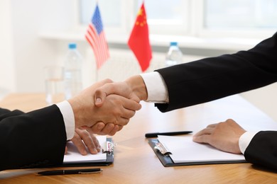 Photo of Diplomats shaking hands during meeting at wooden table indoors, closeup