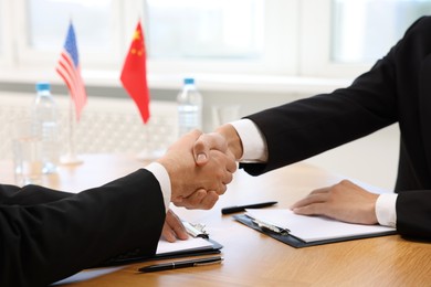 Photo of Diplomats shaking hands during meeting at wooden table indoors, closeup