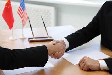 Diplomats shaking hands during meeting at wooden table indoors, closeup