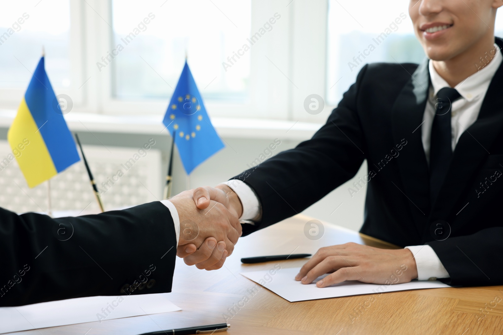 Photo of Diplomats shaking hands during meeting at wooden table indoors, closeup