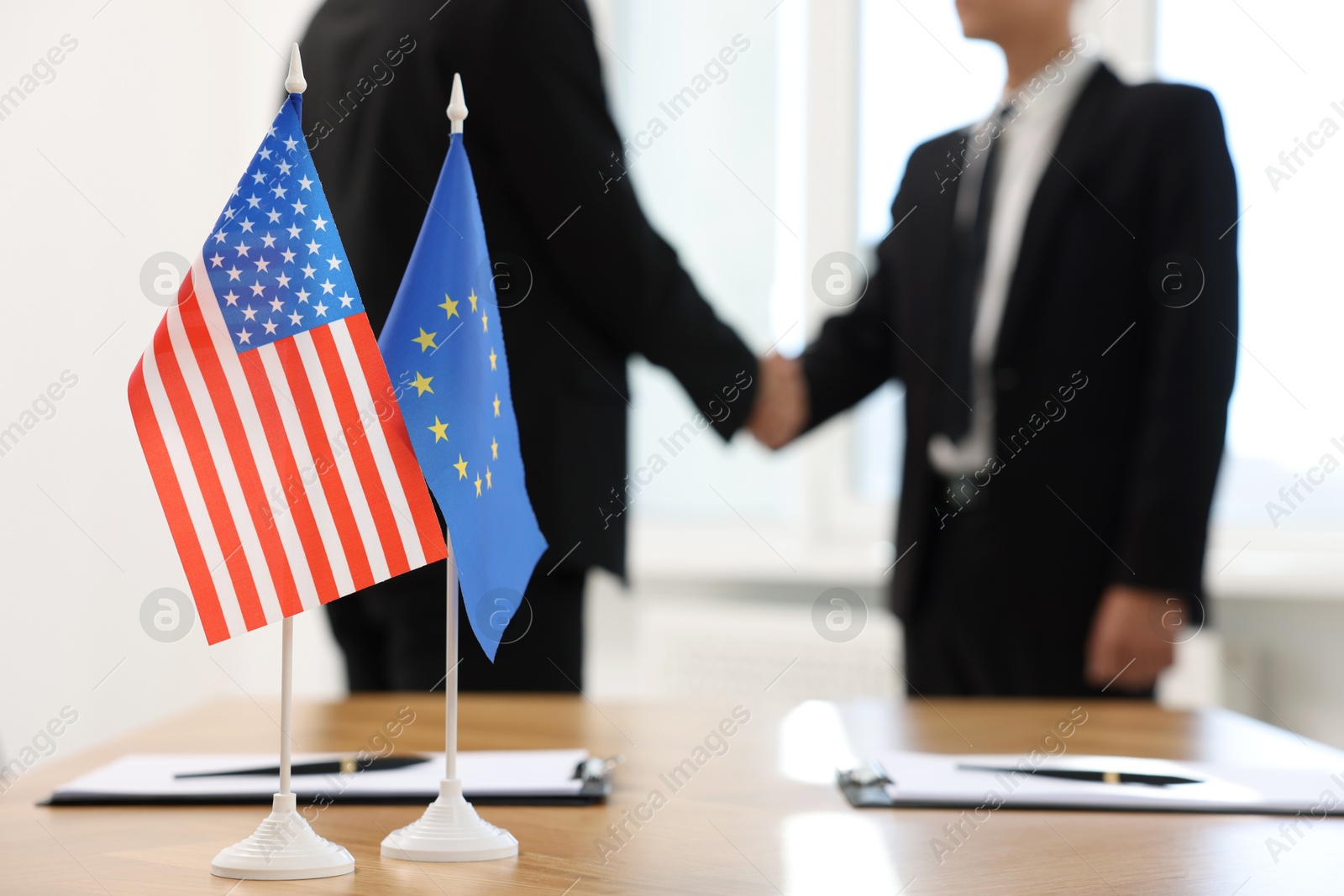 Photo of Diplomats shaking hands during meeting indoors, focus on flags of USA and European Union