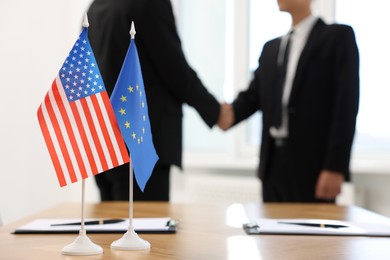 Diplomats shaking hands during meeting indoors, focus on flags of USA and European Union