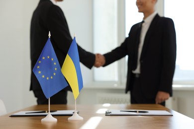 Diplomats shaking hands during meeting indoors, focus on flags of European Union and Ukraine