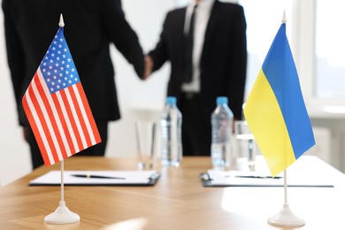 Diplomats shaking hands during meeting indoors, focus on flags of USA and Ukraine