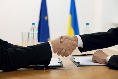 Photo of Diplomats shaking hands during meeting at wooden table indoors, closeup