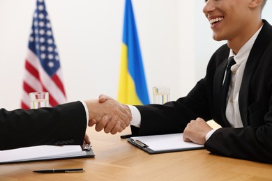 Diplomats shaking hands during meeting at wooden table indoors, closeup