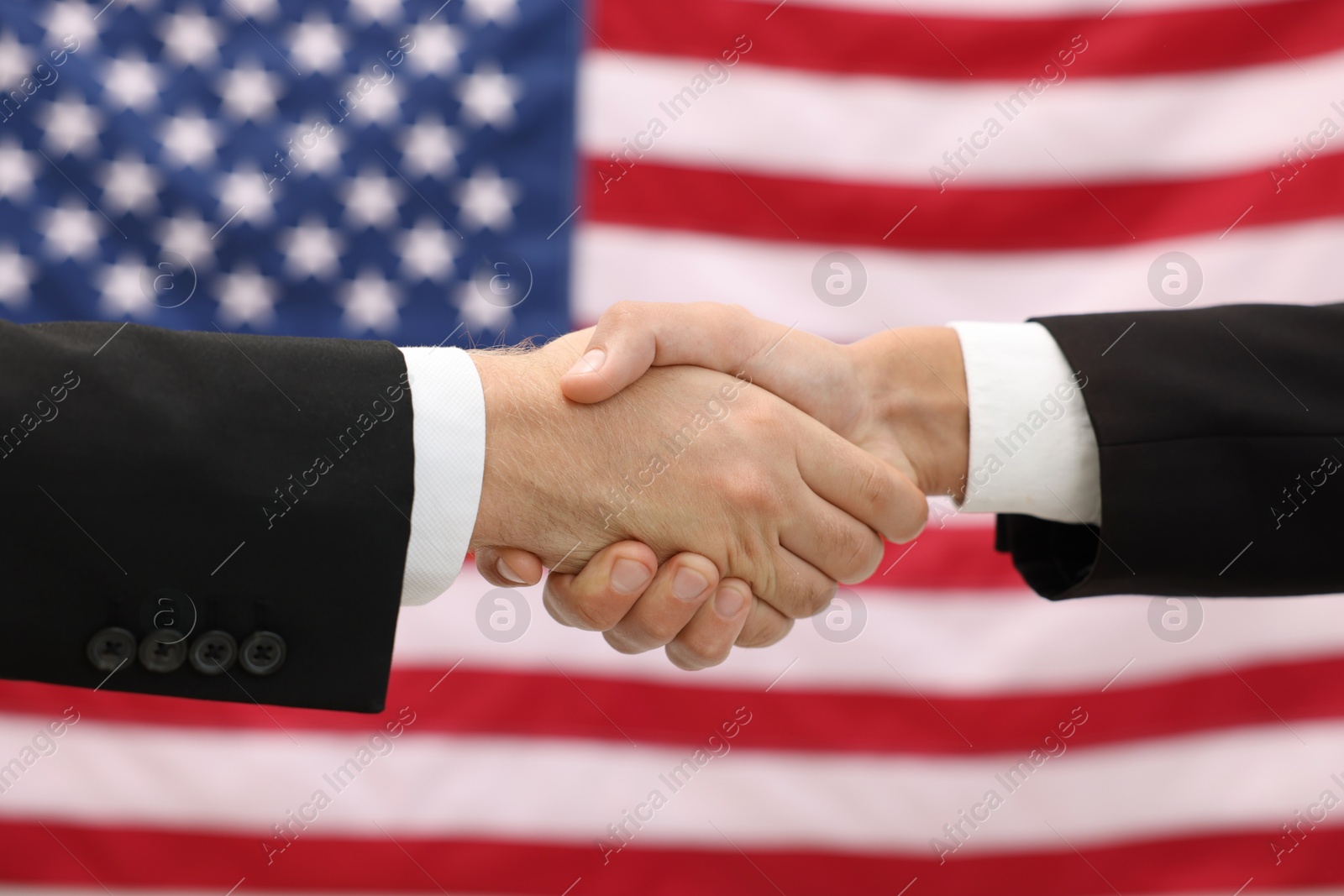 Photo of Diplomats shaking hands against flag of USA, closeup