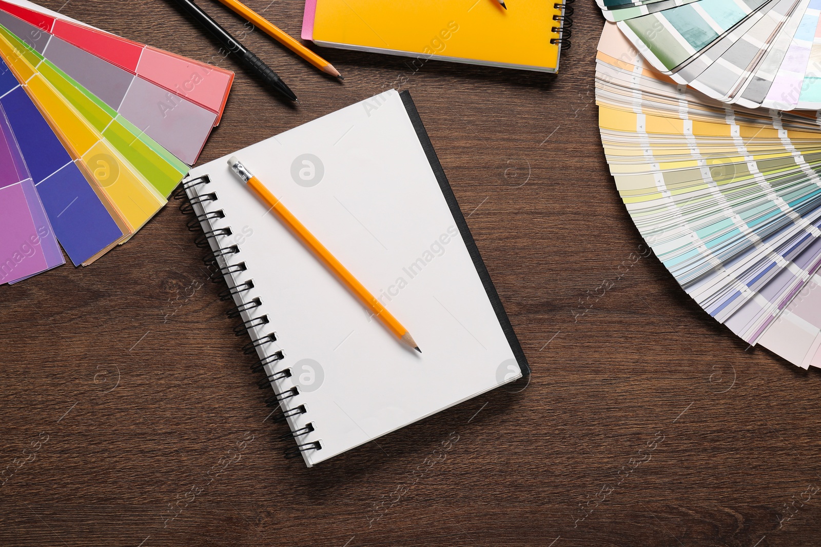 Photo of Color selection charts, notebooks and pencils on wooden table, flat lay. Decorating and design