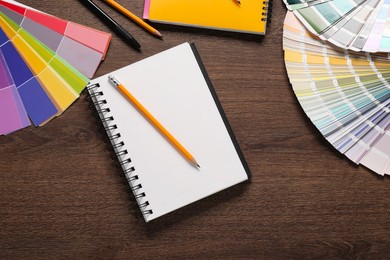 Photo of Color selection charts, notebooks and pencils on wooden table, flat lay. Decorating and design