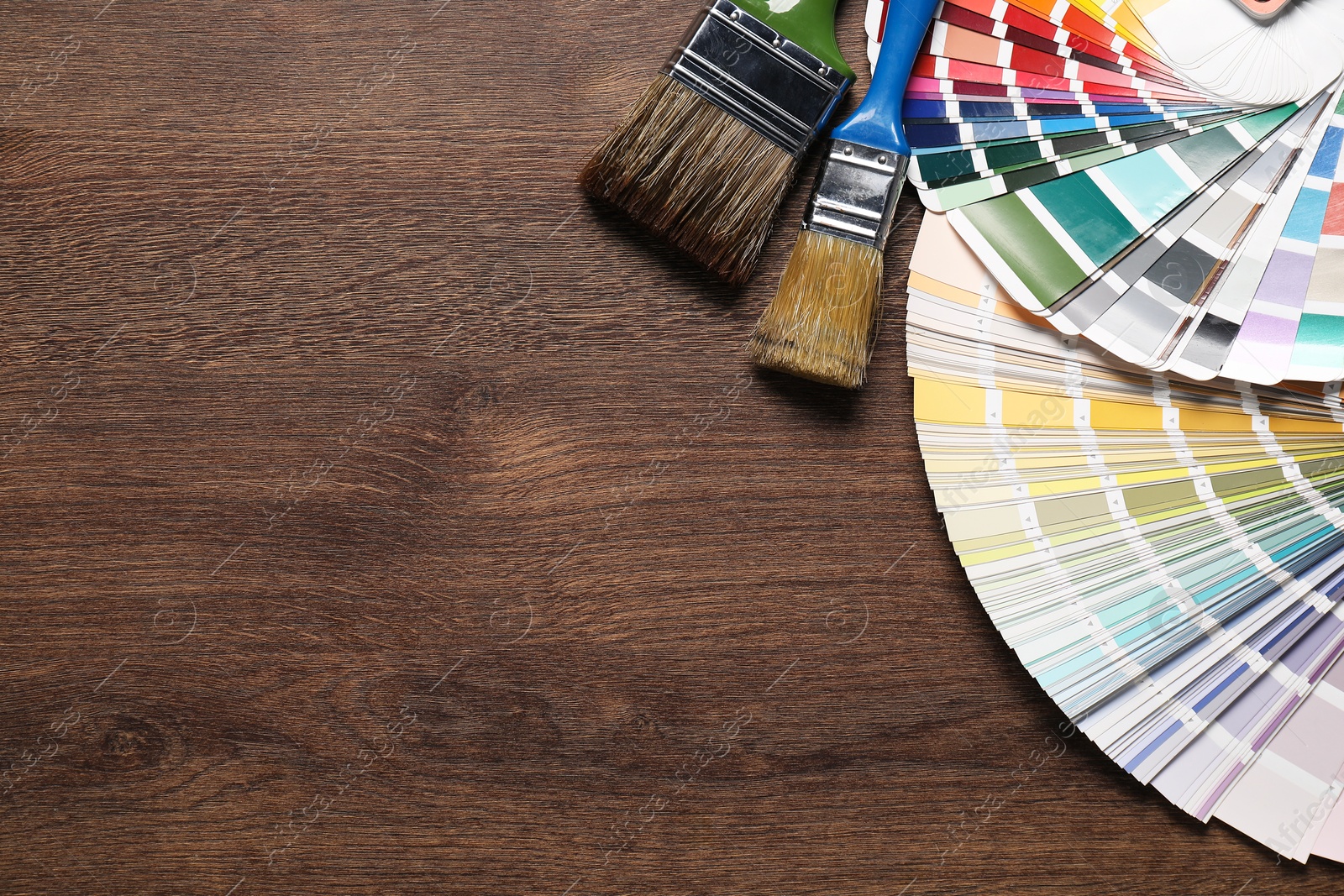 Photo of Color selection charts and paint brushes on wooden table, flat lay with space for text. Decorating and design