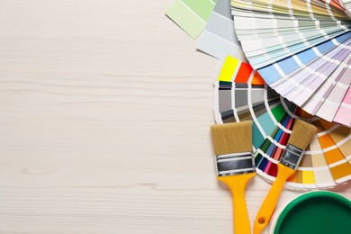 Photo of Color selection charts, paint and brushes on white wooden table, flat lay with space for text. Decorating and design